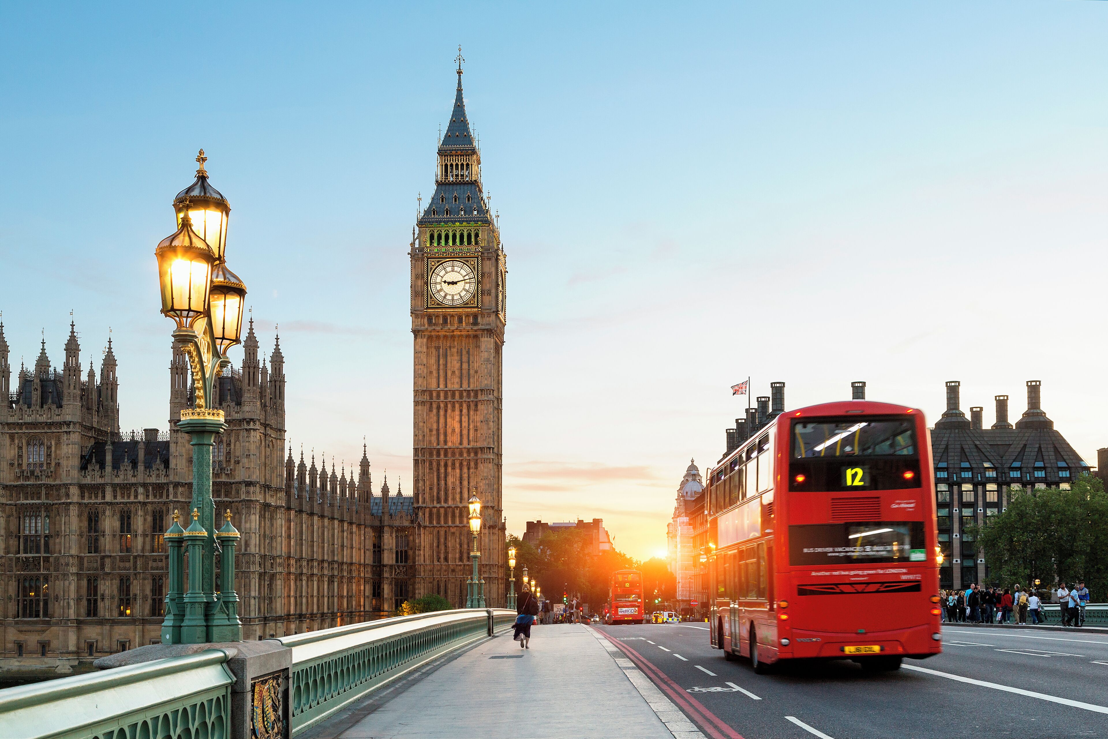 A red double-decker bus on a bridge with the Big Ben in the background.