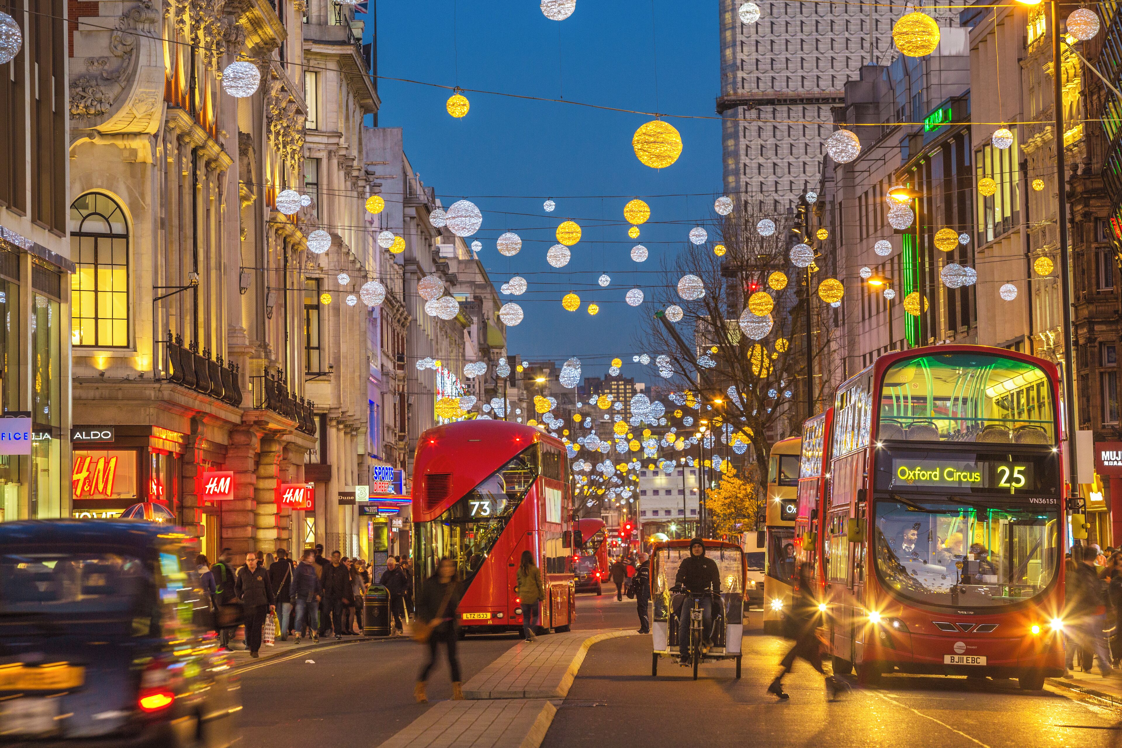 Une scène de rue avec des autobus à deux étages, des piétons et des décorations illuminées.