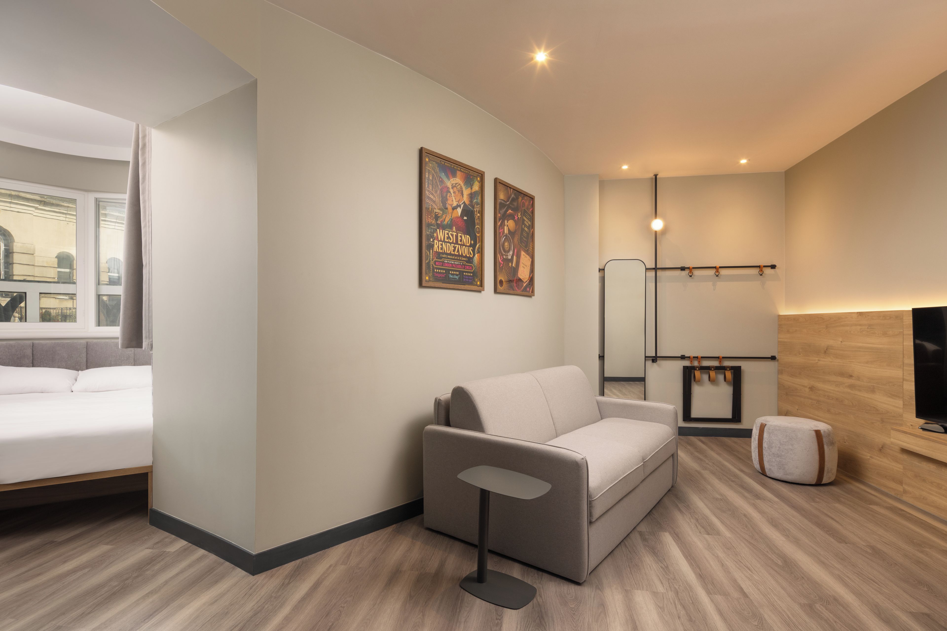 Una habitación de hotel moderna con cama, sofá, una mesita, televisor y dos carteles en la pared.