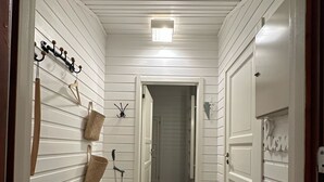 A hallway with white paneling, a black rug, a broom, a basket, hooks, and a door. - Maxi’s Cabin with Sauna and Jacuzzi (Troms)