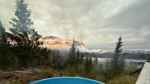 A hot tub on a wooden deck with a view of a mountain and a lake. - Maxi’s Cabin with Sauna and Jacuzzi (Troms)