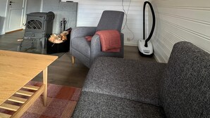 A cozy living room with a fireplace, a comfortable gray sofa, a wooden coffee table, and a flat-screen TV mounted on the wall. - Maxi’s Cabin with Sauna and Jacuzzi (Troms)