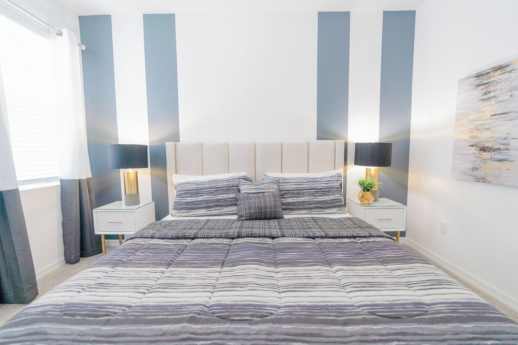Un dormitorio con una cama grande, dos mesitas de noche con lámparas, un velador y un estante en la pared con una planta.
