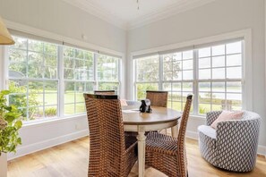 A dining area with wicker chairs and a round table, large windows with a view of greenery, and a white ceiling. - Water's Edge - a lakefront oasis. 10 peaceful, private acres w' stunning views. (Dade City)