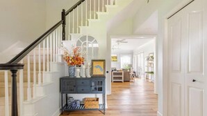 A spacious hallway with a wooden staircase, a blue console table, and a view into the adjacent room. - Water's Edge - a lakefront oasis. 10 peaceful, private acres w' stunning views. (Dade City)