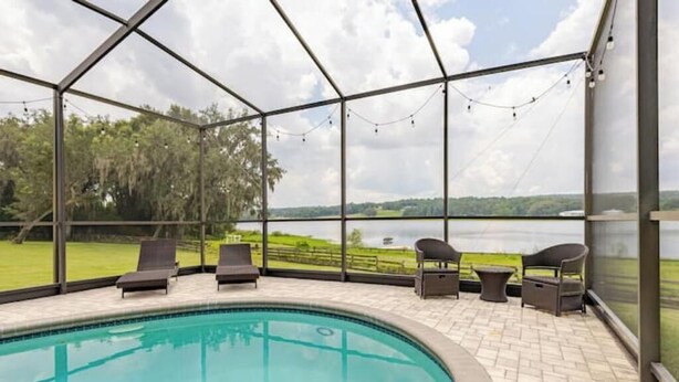 A covered outdoor swimming pool with lounge chairs and a view of a lake. - Water's Edge - a lakefront oasis. 10 peaceful, private acres w' stunning views. (Dade City)