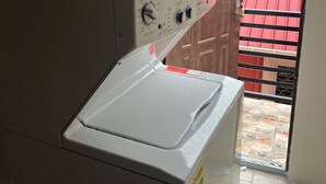 Une buanderie équipée d’un lave-linge et d’un sèche-linge, avec un sol carrelé et une vue sur un bâtiment aux toits rouges à l’extérieur.