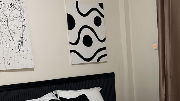 Un lit bien fait, avec une literie blanche et des touches noires, une tête de lit noire et un mur orné d’œuvres d’art abstraites.