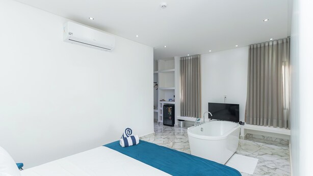 A modern hotel room with a bed, a bathtub, a TV, and a minibar. - Villa Santorini Boutique e Hotel  (Pirenópolis)