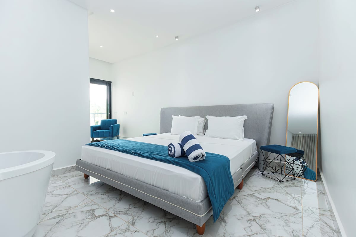 A modern bedroom with a bed, a blue chair, a small table, and a mirror.