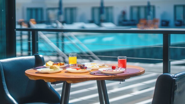 A dining table with breakfast items and drinks on a balcony with a pool view. - Villa Santorini Boutique e Hotel  (Pirenópolis)