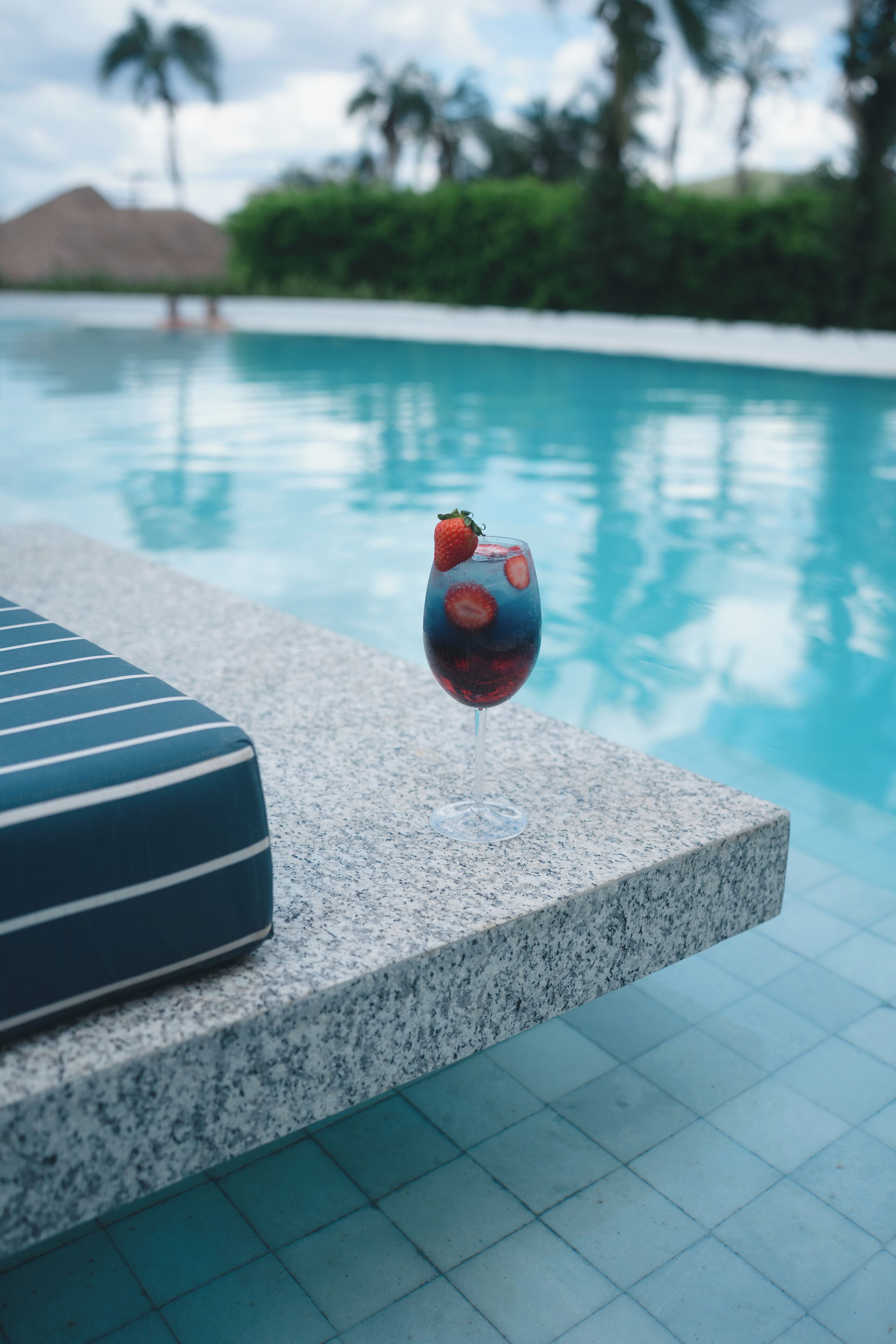 Cenário à beira da piscina, com um copo de bebida vermelha e uma espreguiçadeira listrada.