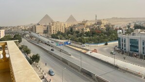 A cityscape with a prominent pyramid structure in the background, modern buildings, and a highway with vehicles. - wake up to the pyramids (Giza)