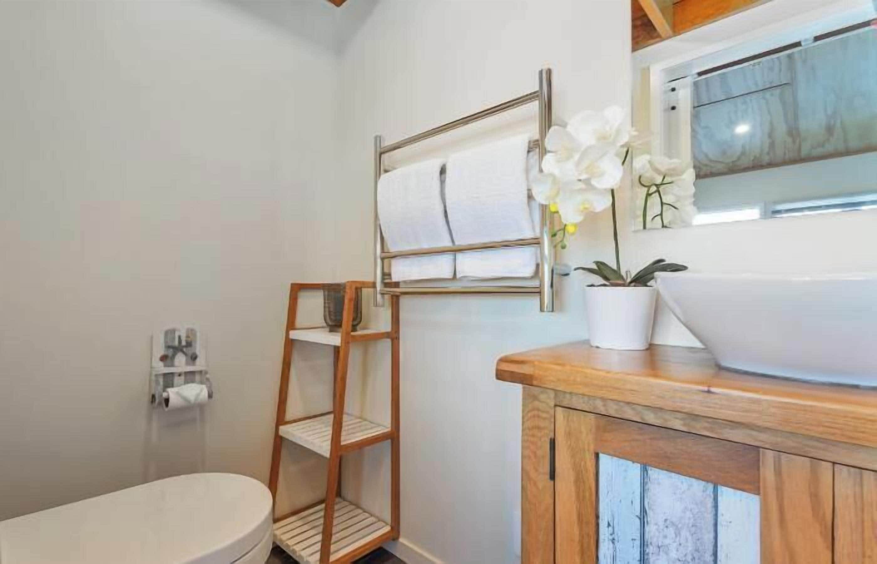 Een badkamer met een wit toilet, een houten plank, een handdoekhouder en een groot wit wastafel op een houten aanrecht.