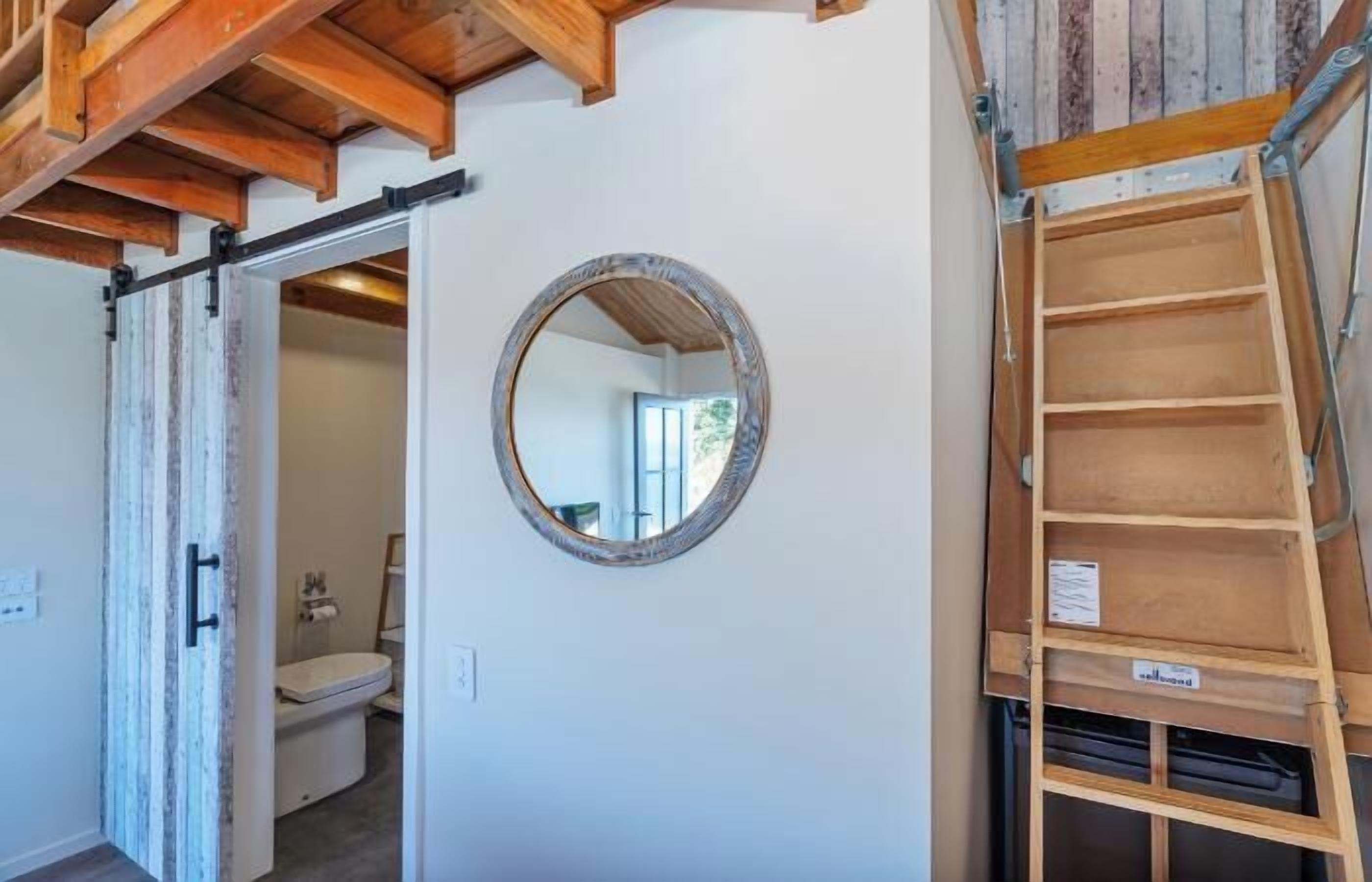 A room with a wooden ladder, a circular mirror, and a sliding door leading to a bathroom.