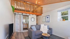 A cozy living room with a grey sofa, a small round table with a drink, and a wooden ceiling. - Oceanview Tiny Home Whiti (Whitianga)