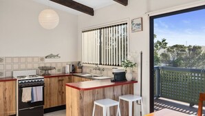 A kitchen with a wooden countertop, a stove, a sink, and a window with vertical blinds. There are two white stools and a potted plant on the counter. - Pacific Chillz in Ulladulla (Ulladulla)