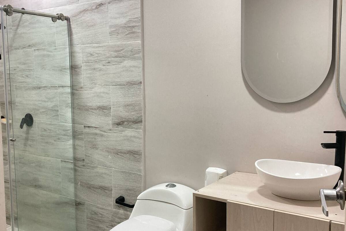 Een moderne badkamer met een douchecabine van glas, een toilet, een wastafel met spiegel en een badkamerkast.