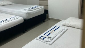 A small, clean room with two single beds, a built-in wardrobe, and a bedside table with a towel and a small item.