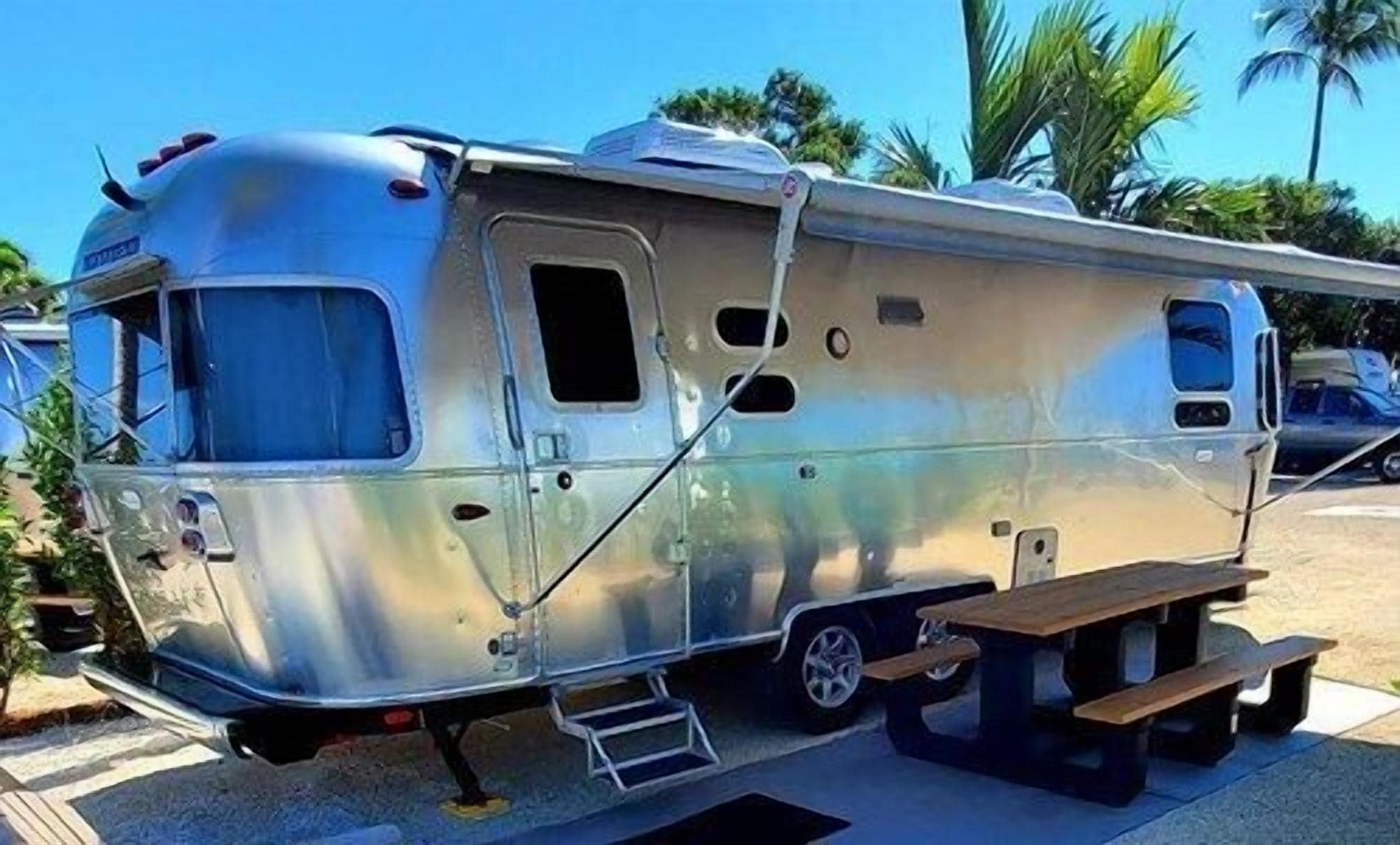 A silver RV with a sliding door, a small window, and a picnic table attached.
