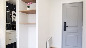 A room with a white door, a radiator, a white cabinet with drawers, and a shelf with a pink orchid.