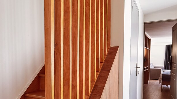 A wooden staircase with a modern design, leading to a room with a bed and a chair.