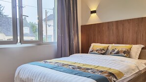 A bedroom with a bed, a window, curtains, a wall-mounted light, and a wooden headboard.