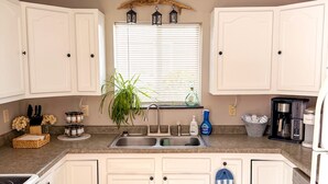 A kitchen with white cabinets, a double sink, a stove, and a blue and white rug. - Lake Superior Stay - Fire Pit Patio - Pet Friendly (Ashland)