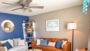A living room with a ceiling fan, a sofa, a coffee table, and a rug. - Lake Superior Stay - Fire Pit Patio - Pet Friendly (Ashland)