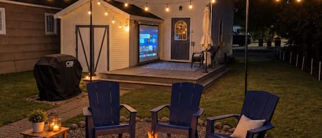 A backyard with a fire pit, outdoor seating, and string lights.