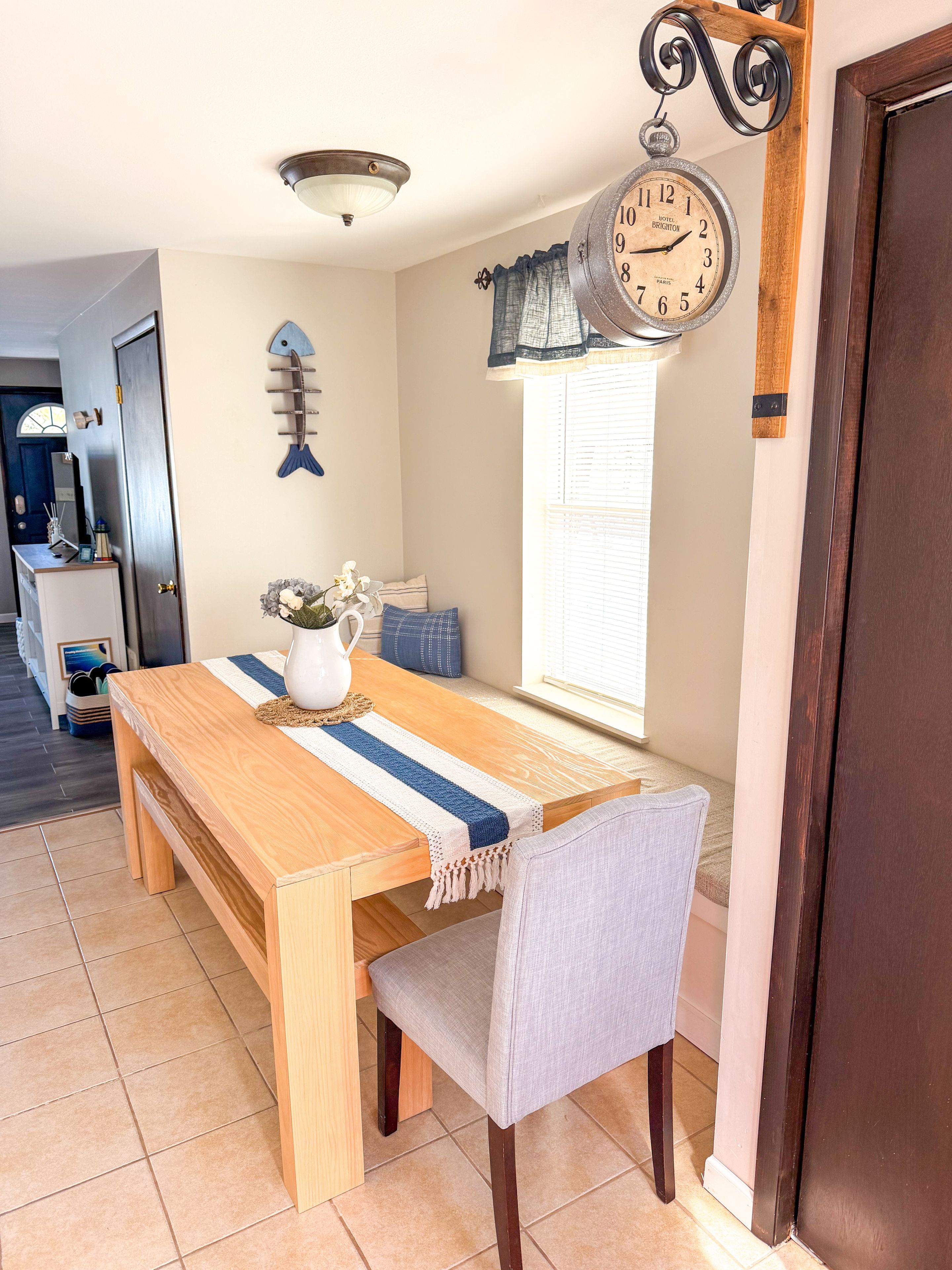 A dining area with a wooden table, a chair, a clock, and a window with blinds.