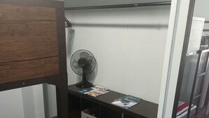 A bedroom with a bunk bed, a desk with a fan, and storage drawers.