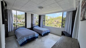 A room with two beds, large windows, a wooden table, and a view of a green landscape. - Apartment with ocean and golf course views (Acapulco de Juárez)