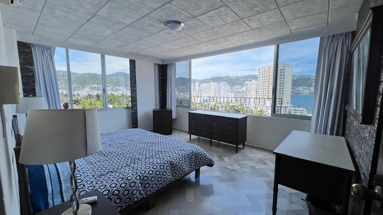 Une chambre d’hôtel avec un grand lit, un bureau, une commode et une vue sur la ville et les collines.