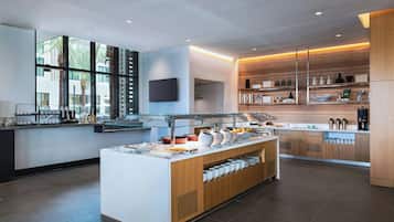 A modern kitchen with a buffet setup, including a central island with food items, a glass display case, and a wooden shelving unit with kitchenware.