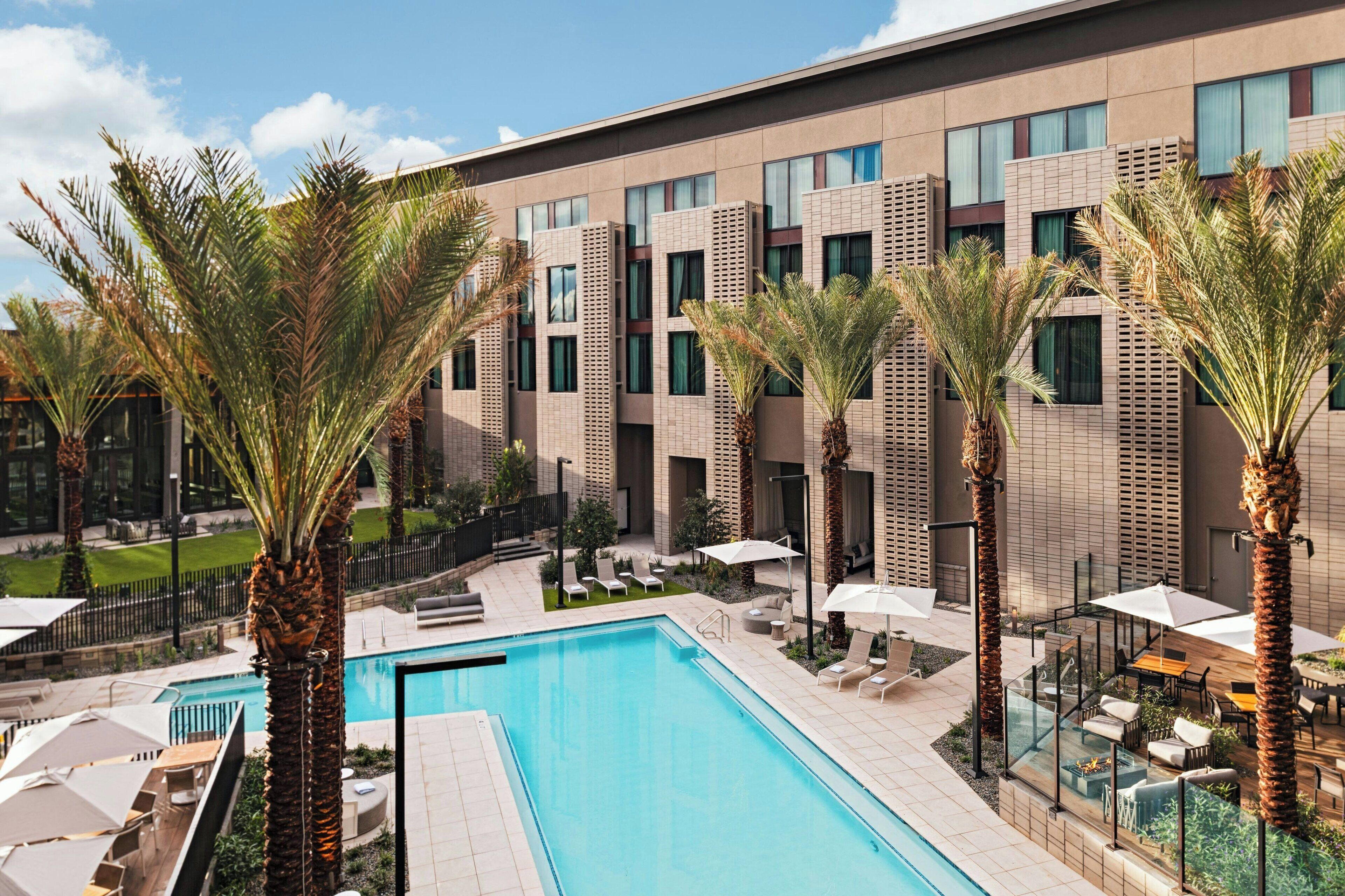 Un hôtel moderne doté d’une piscine, de palmiers et d’espaces de détente en plein air.