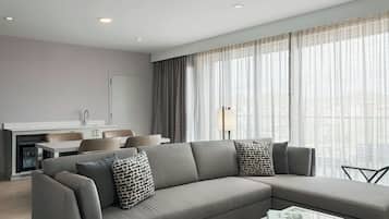 A modern living room with a grey sectional sofa, a glass coffee table, and a view of the city through large windows.