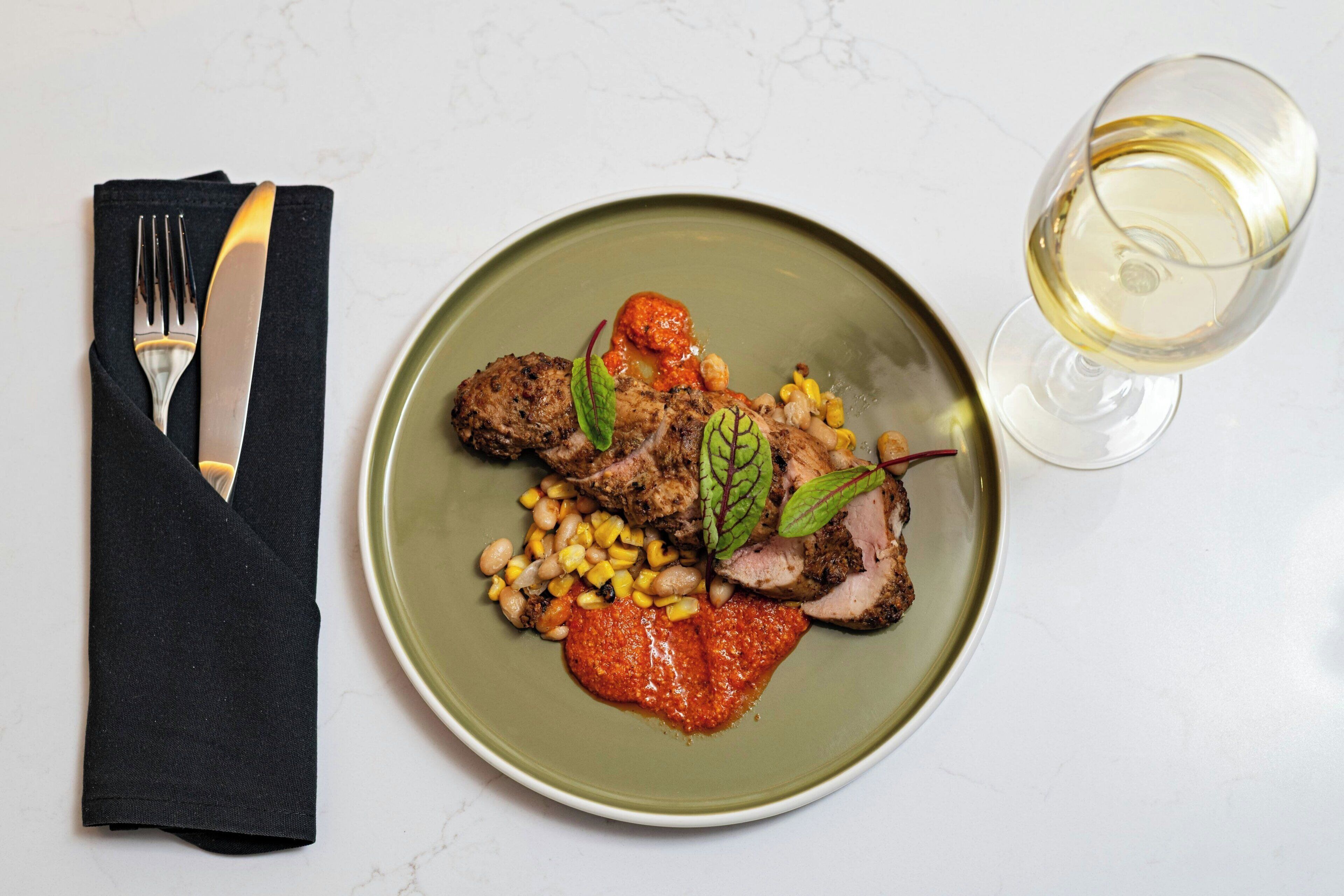 A plate of food with a glass of white wine on a white table.