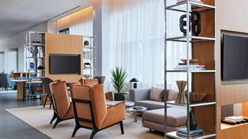 A modern living room with a sofa, chairs, a coffee table, and a TV. There are bookshelves and a plant.
