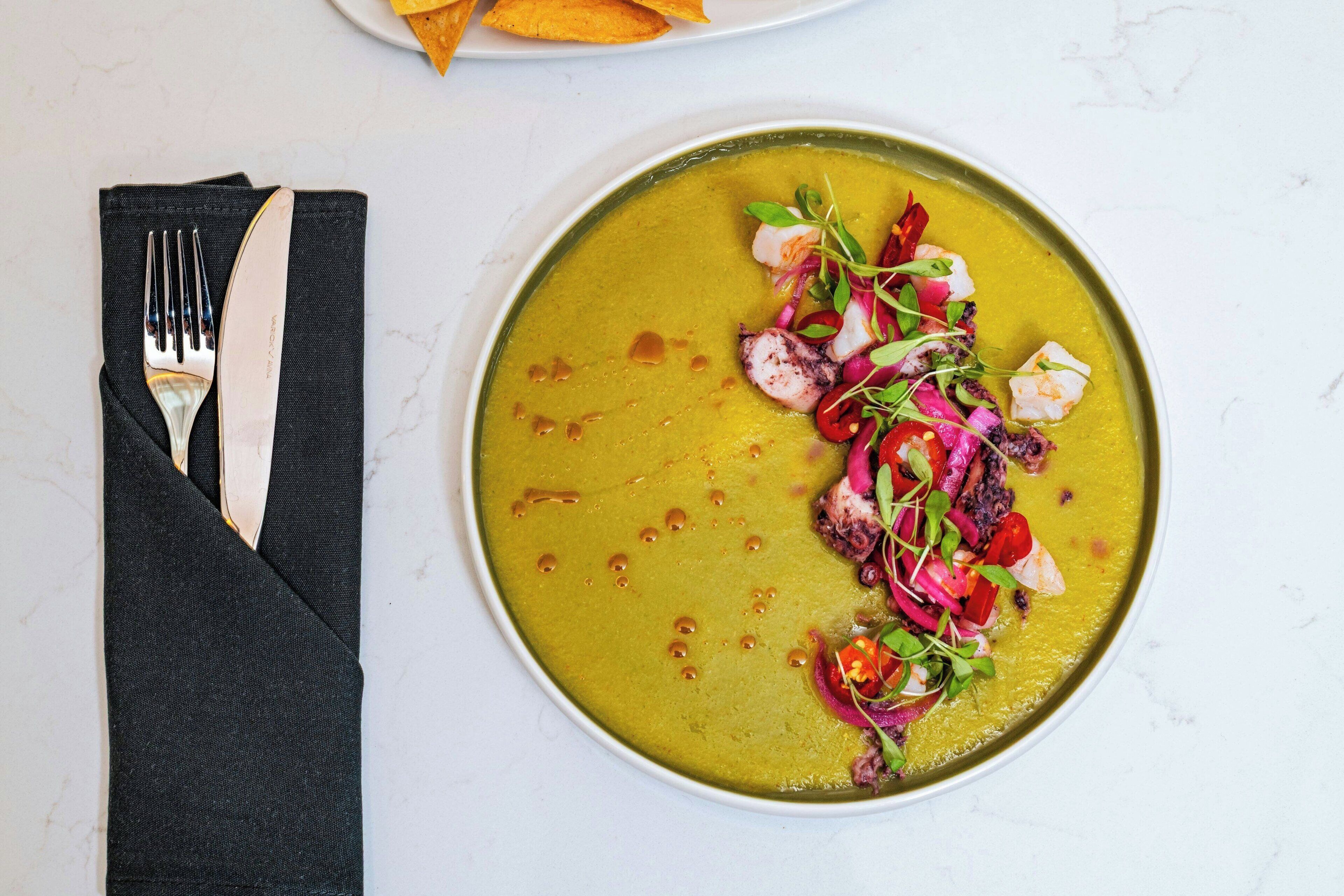A plate of soup with a garnish of vegetables and herbs.