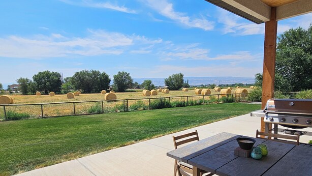 An outdoor patio with a wooden table and chairs, a grill, and hay bales in the background. - Experience Desert Gemini Ranch and the magic of the Colorado high desert (Fruita)