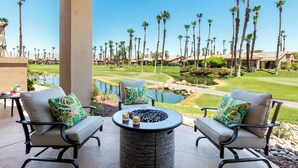 A patio area with two chairs and a round table, overlooking a golf course and a body of water.