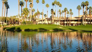 A golf course with a water feature, palm trees, and a building with multiple floors.