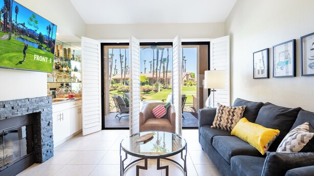 A living room with a fireplace, a glass coffee table, a sofa with cushions, and a TV displaying a golf course.
