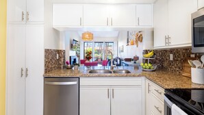 A modern kitchen with white cabinets, a granite countertop, stainless steel appliances, and a view of the outdoors through large windows.