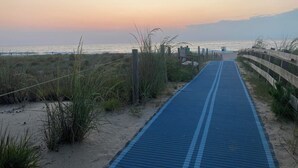 Un paseo marítimo costero con una valla de madera a un lado y una playa arenosa al otro, que se dirige hacia el mar.