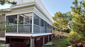 Una casa de dos pisos con balcón, terraza de madera y un pequeño puente que conduce a la entrada.