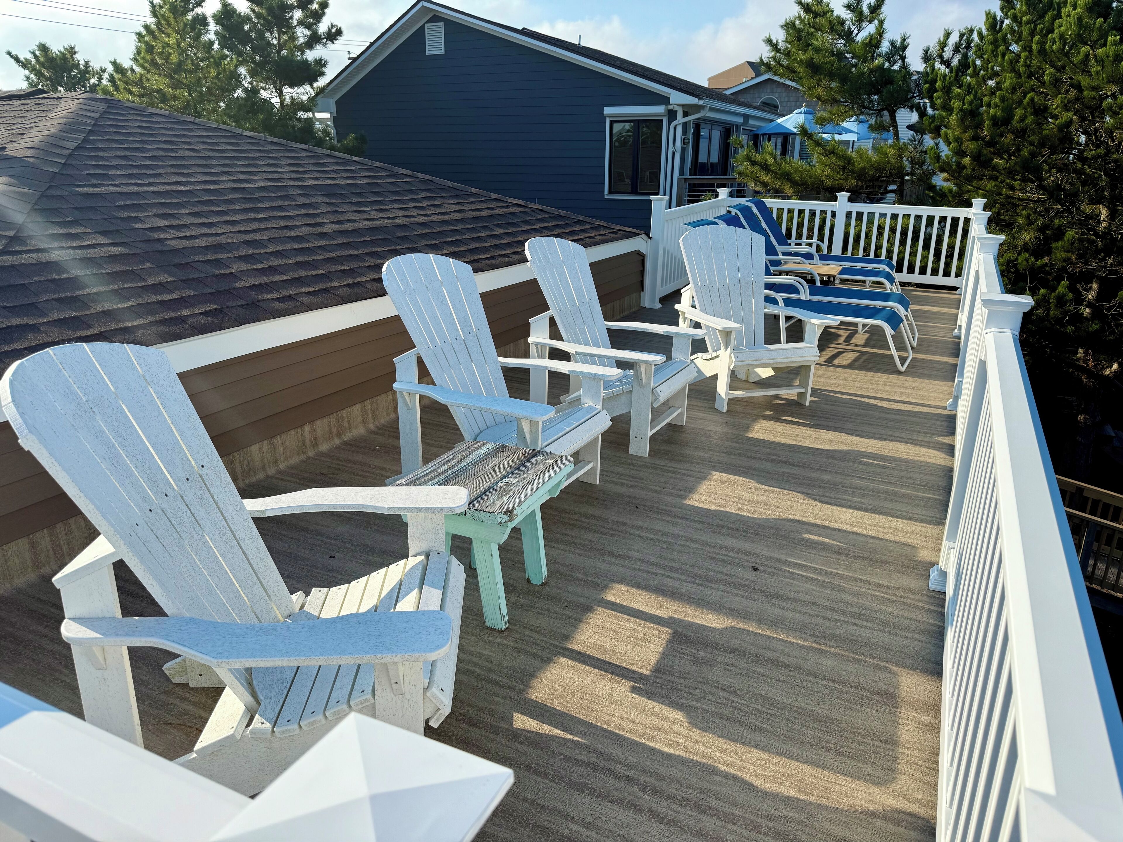 Terraza exterior cubierta con sillas Adirondack y baranda blanca.