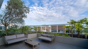 A rooftop terrace with a grey sofa set, a wooden coffee table, and various potted plants. - Studio Just a few Steps From the Beach - Kpl0806 (Sao Jose)