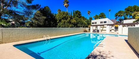 A rectangular swimming pool with clear blue water, surrounded by a concrete deck and a low stone wall.